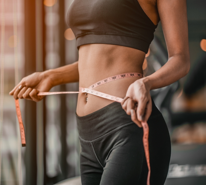 Young slim woman tape after a diet with accessory in sporty gym as background.